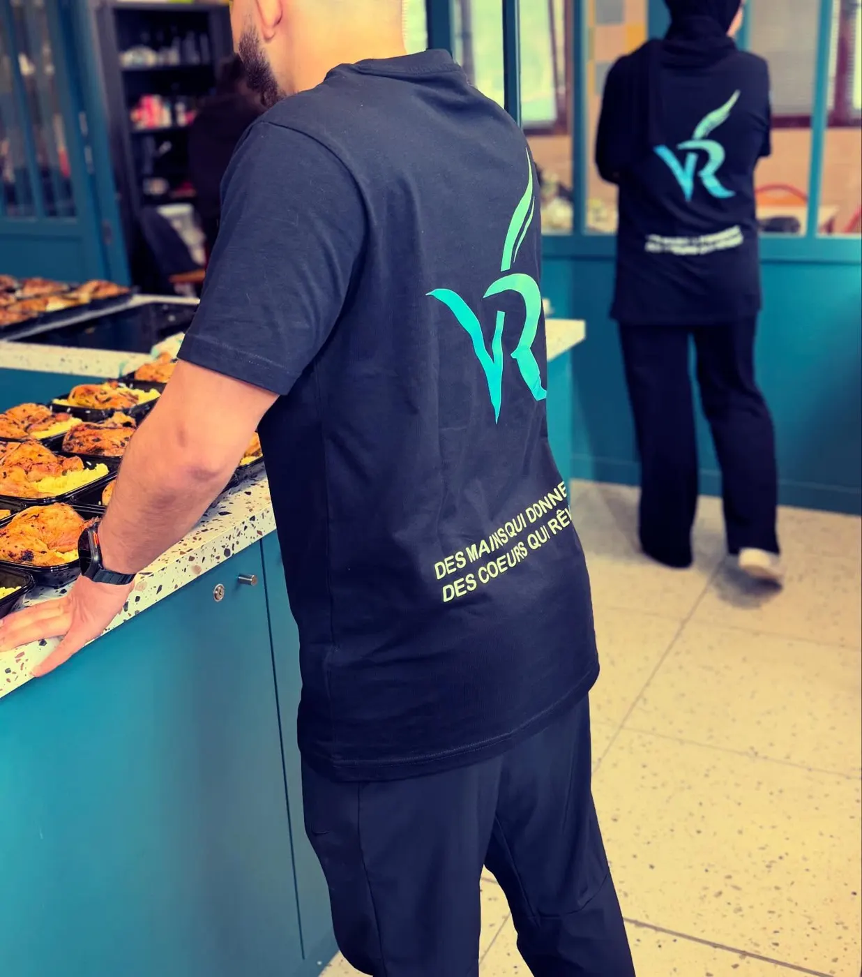 Deux bénévoles de VivoRêve en cuisine, dos au logo VR