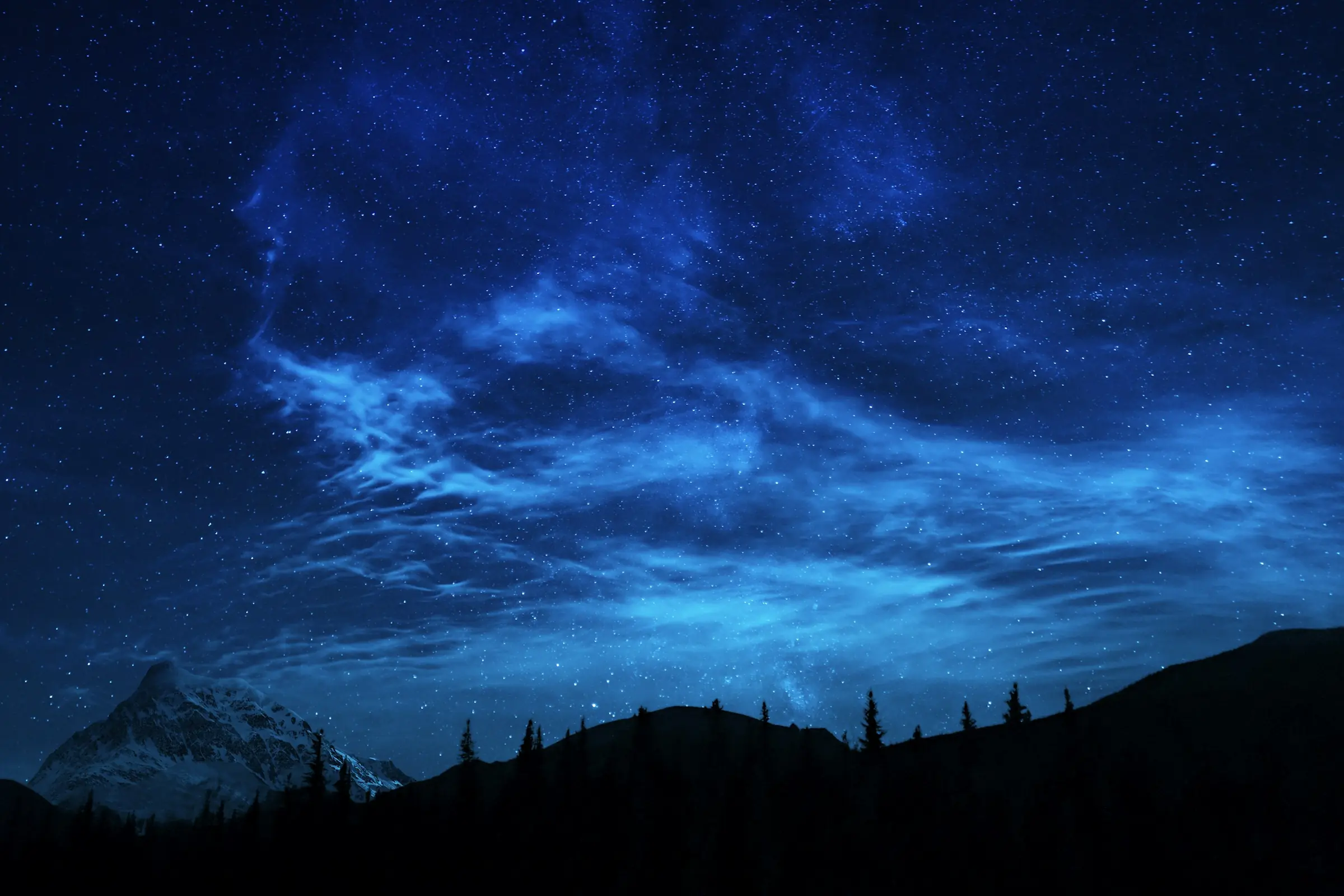 Un ciel de nuit bleu, des nuages lumineux et des étoiles au-dessus des montagnes